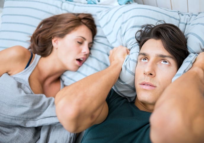 Snoring woman fast asleep while her partner is wide awake and aggravated