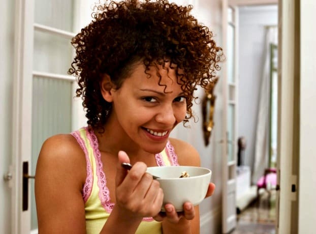 Smiling woman eating bowl of cereal not taking too many vitamins during pregnancy