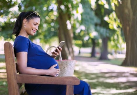Pregnant woman looks at her phone while sitting on a park bench