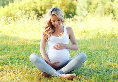 Happy young pregnant woman sitting on grass doing yoga in her maternity athleisure clothes