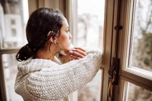 Young woman looks out her window, pregnant and alone