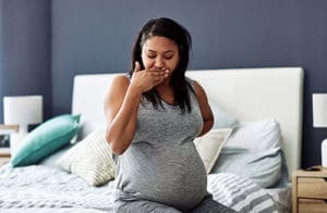 Woman with Hyperemesis Gravidarum late into her pregnancy sitting on her bed and trying not to throw up