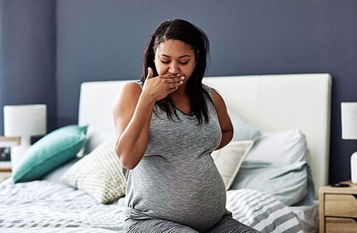 Woman with Hyperemesis Gravidarum (HG) late into her pregnancy sitting on her bed and trying not to throw up