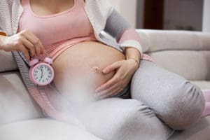 Cropped shot of a very pregnant woman holding an alarm clock