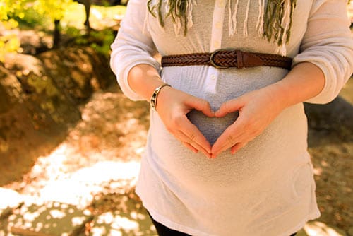 Pregnancy help for this woman striving for a stress-free pregnancy makes a heart with her hands over her pregnant belly