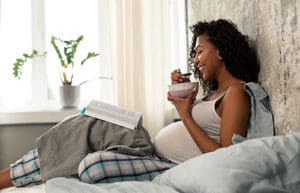 Pregnant woman eating oatmeal while reading in bed