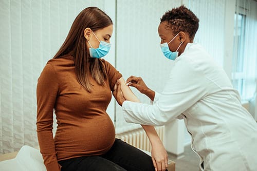 female doctor preparing a pregnant woman for COVID-19 vaccine shot