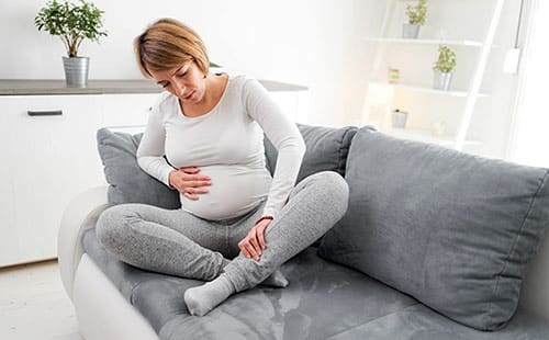 Woman at home on her sofa suffering from leg cramps during pregnancy