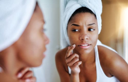 Young woman inspecting her skin in front of the bathroom mirror and wondering about pregnancy-safe skincare