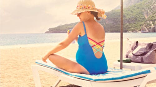 Pregnant woman relaxing on the beach, applying a pregnancy-safe sunscreen