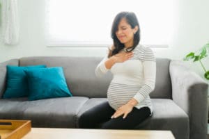 Woman sitting on her sofa while she experiences the discomfort of pregnancy heartburn