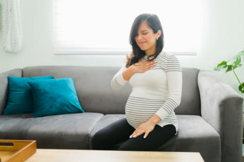 Woman sitting on her sofa while she experiences the discomfort of pregnancy heartburn