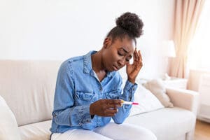 Worried African American woman checking her recent pregnancy test, sitting on couch at home