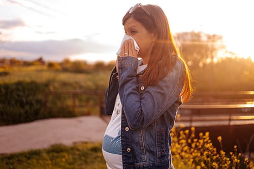 Woman in a park experiencing a stuffy nose during pregnancy wiping her nose