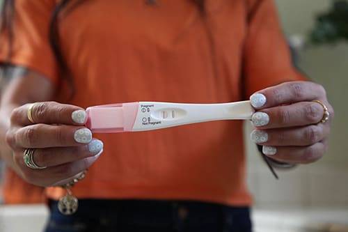 An unrecognizable woman in an orange shirt holding up a positive pregnancy test