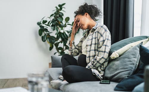 African American woman seated on her couch experiencing forgetfulness during pregnancy