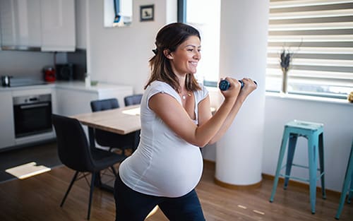 Expecting mother lifting hand weights as part of her pregnancy exercises at home