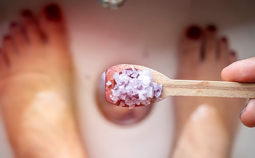 Woman pouring Epsom salt from small wooden spoon into her bath