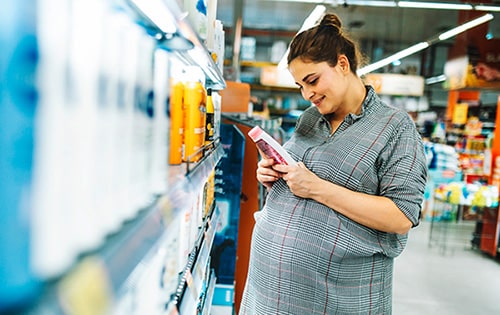 Smiling pregnant woman reads the ingredient list on a shampoo bottle in a grocery store