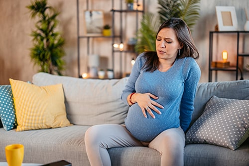 Young pregnant woman having Braxton-Hicks contractions while seated on her sofa