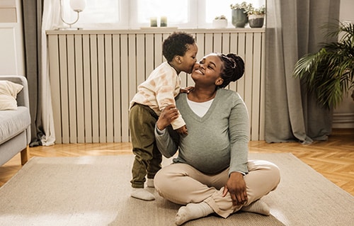 Expecting mother receives a kiss from her toddler son while seated in her living room